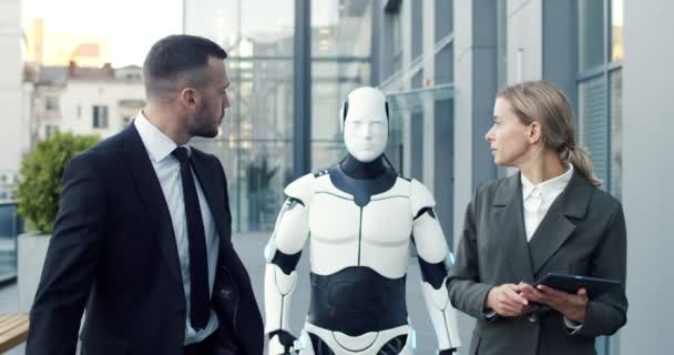 Hombre de negocios en traje hablando con su colega en la calle. Mujer que usa tableta mientras maneja droide y le dice algo a su pareja masculina. Innovaciones y concepto de ciberandroide — Vídeos de Stock