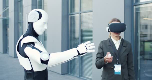 Młoda bizneswoman w wirtualnej rzeczywistości stoi na ulicy przed robotem i zarządza nim. Okulary VR social network koncepcja robota — Wideo stockowe