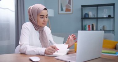 Müslüman öğrenci odada ders çalışıyor, dizüstü bilgisayar ve not defteri kullanıyor. Sınavlara hazırlanan tesettürlü Arap bir kadın. Sıcak sarı fincandan çay içen bir kadın. Üniversite yaşam tarzı, İslam konsepti