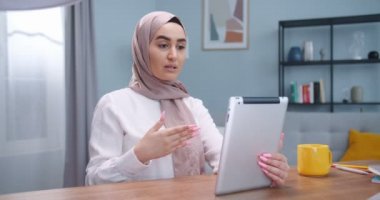 Yakından bakınca, tesettürlü genç Arap kadın portresi odada oturan tablette bir video çağrısı var. İnternette arkadaşlarıyla duygusal konuşmalar yapan Arap bir kadın. Yaşam tarzı, modern İslam kavramı..