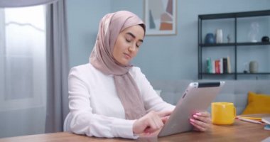 Mutlu Müslüman kadının tesettüre girip rahat bir odada oturması dijital tablet kullanması, gülümsemesi, daktilo etmesi, internette arama yapması. İnternette neşeli bir bayan mesaj arkadaşı. Teknoloji kavramı