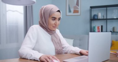 Heyecanlı genç Müslüman kadın kazanan dizüstü bilgisayara bakıyor ve evde online başarısını kutluyor. Öforik kadın yeni bir iş fırsatı elde ediyor, e-postada iyi haberler okuyor, zafere seviniyor, motive oluyor..