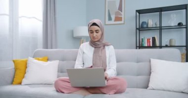 Karantinada bilimsel makaleler yazan tesettürlü genç Müslüman kız öğrencilerin orta planı. Çevrimiçi uzaklık kursunda çalışan bir kadın yeni bir meslek öğreniyor. Kanepede otururken online kurs alıyor.