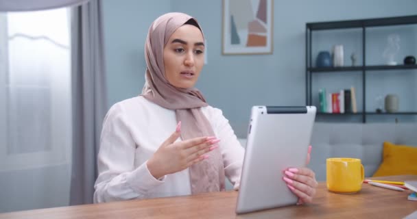 Closeup side view portrait of young arabian female in hijab having a video call on the tablet sitting in the room. Arab woman emotionaly speaking with friends online. Lifestyle, modern islam concept. — Stock Video