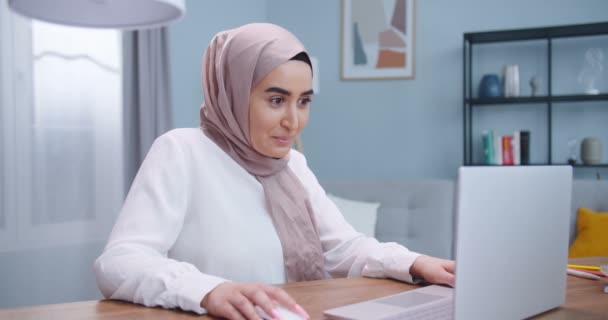 Excited young muslim woman winner looks at laptop celebrates online success at home. Euphoric lady gets new distance job opportunity, reads good news in email, rejoices victory, feels motivated. — 图库视频影像