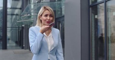 Genç, şık ve güzel bir iş kadını, açık havada yürüyen, ona bir sesli mesaj dikte eden ve neşeyle gülümseyen..