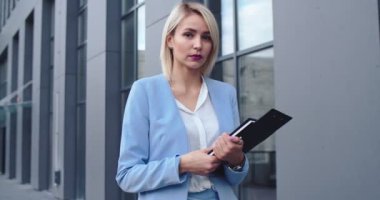 Dosyada yazılı evrakları olan, avukat ya da şirketin CEO 'su olarak kameraya poz veren güzel sarışın beyaz iş kadınının portre fotoğrafı. Dışarıda..