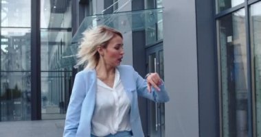 Kafkasyalı genç sarışın iş kadını elinde evrak klasörüyle modern ofis binasında caddeyi yönetiyor ve saate bakıyor önemli bir iş toplantısına geç kalmış gibi görünüyor..