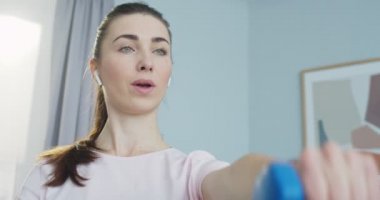 Salonda akıllı kaslar için halterlerle kol egzersizi yapan kulaklıklı bayan sporcuların portresini yakın çekime alın. Spor ve spor. Eğitim, egzersiz ve sağlık..