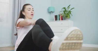 Genç ve formda bir kadının egzersiz yapması ve modern iç mimarisi olan rahat dairesinde beyaz kulaklıklarla müzik dinlemesi. Formda bir kadın karın kası egzersizi yapıyor. Evde bacaklarını esnetiyor..