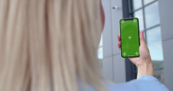 Lvov, Ukrajina - 02.10.2019: Zadní strana blonďaté bělošky, která drží smartphone se zelenou obrazovkou a sleduje pohyb, jako by se na něco dívala, Venku. Chromatický klíč. Prázdné místo pro vaše reklamy. — Stock video