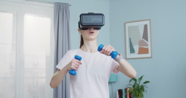 Close up of young woman training at home and wearing virtual reality goggles while performing box and using dumbbells. Healthy lifestyle and vr simulation concept. Sport and fitness. — 图库视频影像