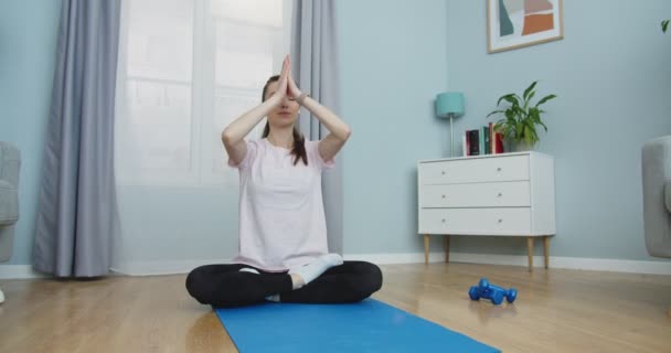 Middle plan of carefree beautiful woman meditation with closed eyes and arm overhead on mat at home listening to meditation in white headsets. Female doing yoga at home. Active lifestyle concept. — Vídeo de Stock