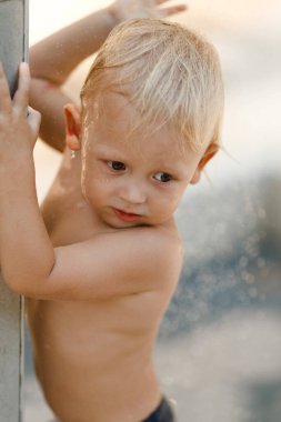 Sarışın çocuk dışarıda duşun altında duruyor.