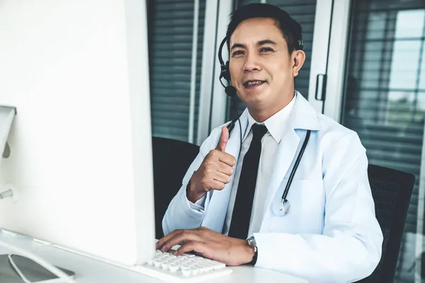 Médico con auriculares hablando activamente en una videollamada en una clínica u hospital . —  Fotos de Stock