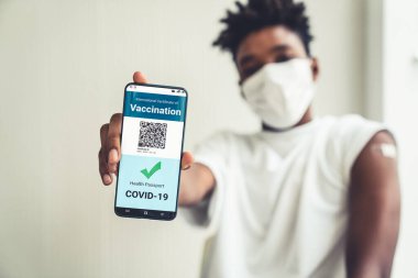 Afrikalı Amerikalı genç cep telefonunda aşı pasaportu gösteriyor