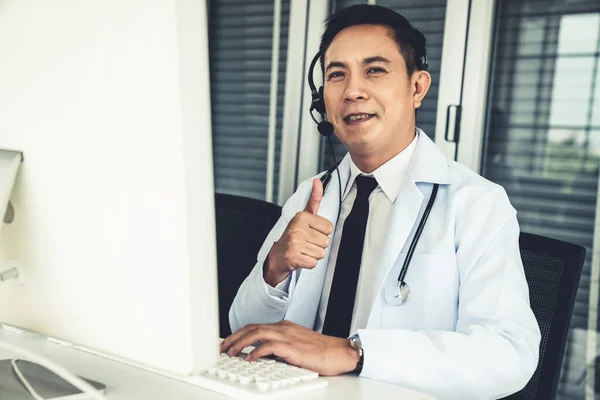 Médico con auriculares hablando activamente en una videollamada en una clínica u hospital . —  Fotos de Stock