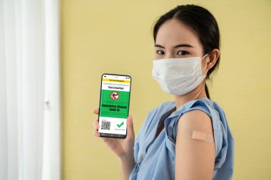 Genç Asyalı kadın cep telefonunda aşı pasaportu gösteriyor.