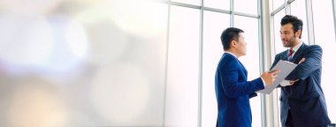 İki iş adamı, ofiste geniş bir bakış açısıyla proje stratejisi hakkında konuşuyor