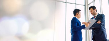 İki iş adamı, ofiste geniş bir bakış açısıyla proje stratejisi hakkında konuşuyor