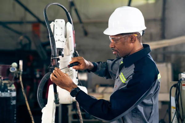 Ouvrier d'usine afro-américain travaillant avec un bras robotique compétent — Photo