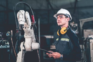 Genç fabrika işçisi usta bir robot kolla çalışıyor.