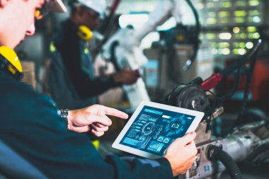 Fabrika işçileri bir atölyede usta robot kolla çalışıyorlar.