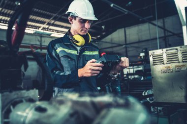 Genç fabrika işçisi usta bir robot kolla çalışıyor.