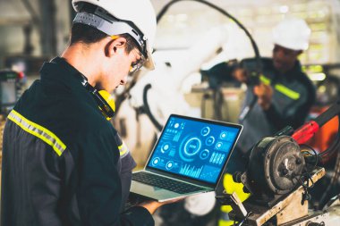 Genç fabrika işçisi usta bir robot kolla çalışıyor.