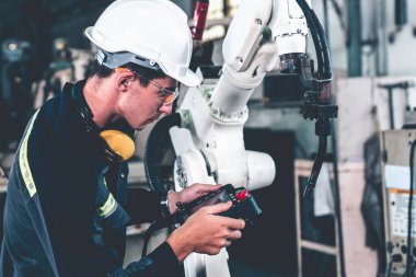 Genç fabrika işçisi usta bir robot kolla çalışıyor.