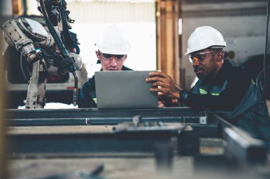 Fabrika işçileri bir atölyede usta robot kolla çalışıyorlar.