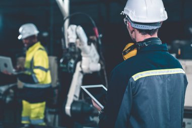 Fabrika işçileri bir atölyede usta robot kolla çalışıyorlar.