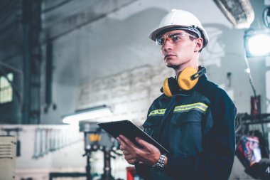 Bir atölye binasında usta tablet bilgisayar kullanan genç bir fabrika işçisi.