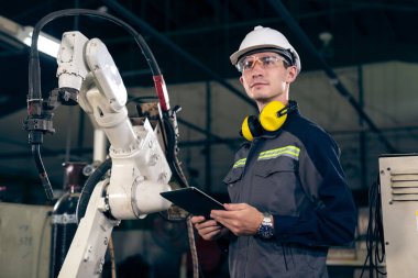 Genç fabrika işçisi usta bir robot kolla çalışıyor.