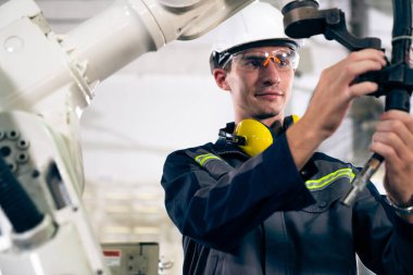 Genç fabrika işçisi usta bir robot kolla çalışıyor.