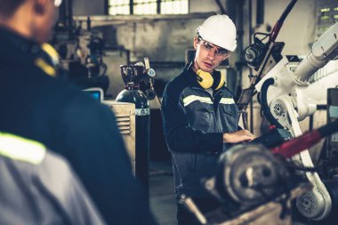 Fabrika işçileri bir atölyede usta robot kolla çalışıyorlar.
