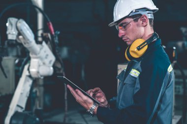 Genç fabrika işçisi usta bir robot kolla çalışıyor.