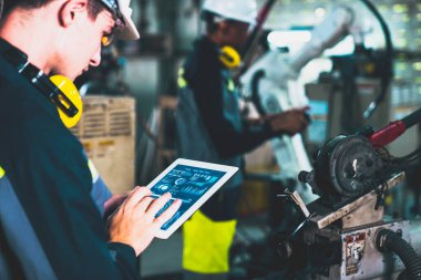 Fabrika işçileri bir atölyede usta robot kolla çalışıyorlar.