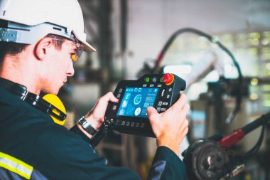 Genç fabrika işçisi usta bir robot kolla çalışıyor.