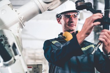 Genç fabrika işçisi usta bir robot kolla çalışıyor.