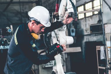 Genç fabrika işçisi usta bir robot kolla çalışıyor.