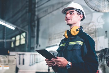 Bir atölye binasında usta tablet bilgisayar kullanan genç bir fabrika işçisi.