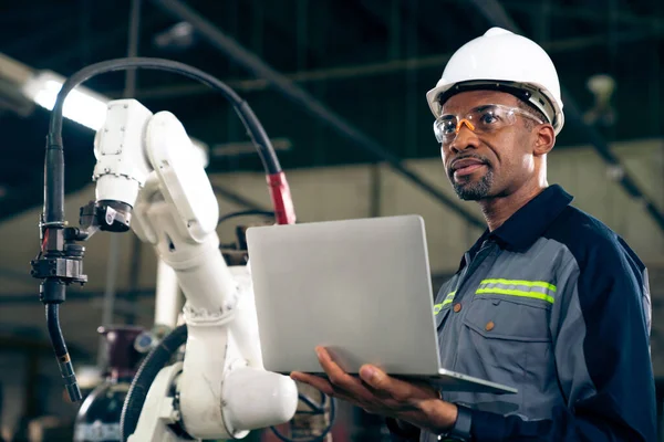 Trabajador de fábrica afroamericano trabajando con brazo robótico adepto — Foto de Stock