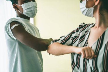 Yüz maskesi takan gülümseyen gençler dirseklerini vurarak sevinçle selamlıyorlar.