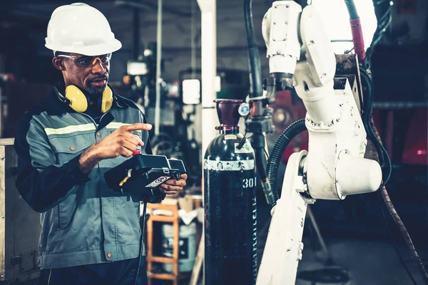 Ouvrier d'usine afro-américain travaillant avec un bras robotique compétent — Photo