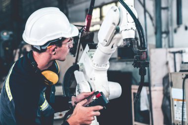 Genç fabrika işçisi usta bir robot kolla çalışıyor.