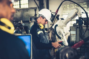 Fabrika işçileri bir atölyede usta robot kolla çalışıyorlar.