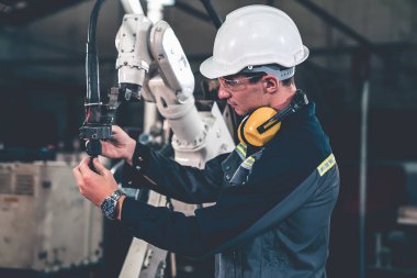 Genç fabrika işçisi usta bir robot kolla çalışıyor.