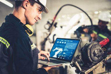 Genç fabrika işçisi usta bir robot kolla çalışıyor.