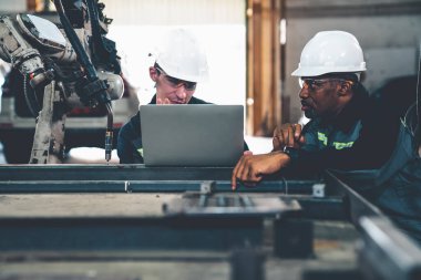 Fabrika işçileri bir atölyede usta robot kolla çalışıyorlar.